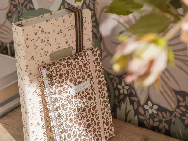 blomstrete notatbøker på hylle med blomstrete tapet bak