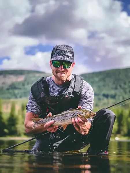 Mann sitter på kne i vannet og holder en fisk