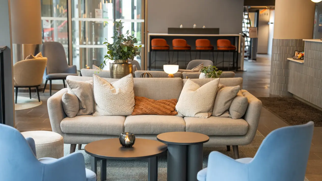 Beige sofa, sofabord, og blå lenestoler i lobby.