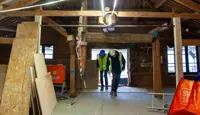 Takmøne, vinduer og vinnehjul sett innenfra i Kjøpmannsgata 15 i Trondheim under oppussing. Bygningsmaterialer på gulvet. Ståle og Trond Are kommer inn fra stillaset.