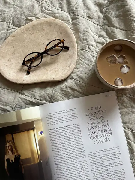 Solbriller på et fat sammen med et magasin og kopp med iskaffe