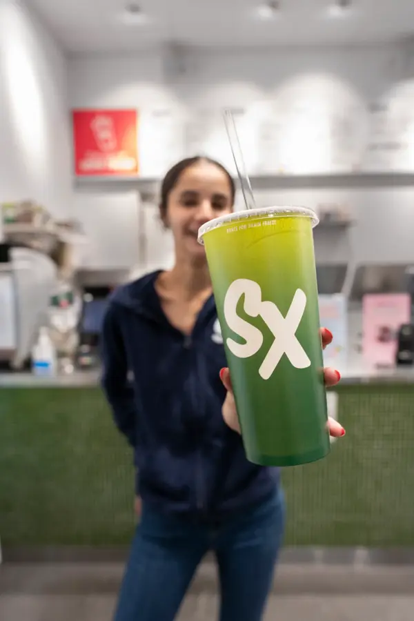 Jente som holder frem et beger med Smoothie fra SmoothieXchange 