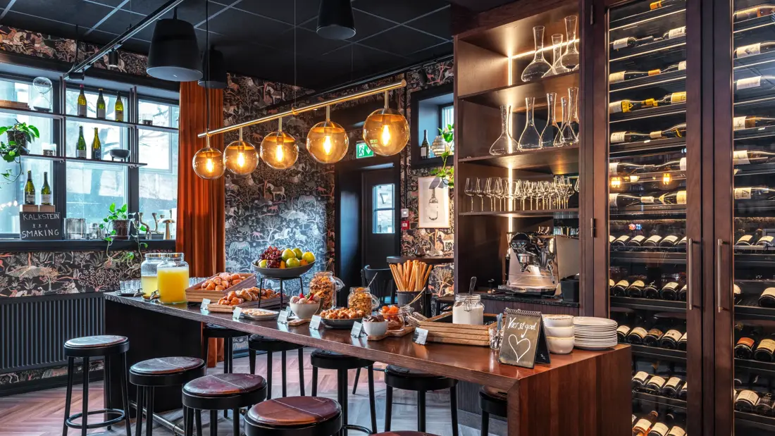 Pausebuffet i Grotten øl- og vinbar, med høye stoler rundt bordet, vinskap i bakgrunnen, taklampe med fem store lyspærer over.