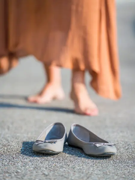 Nærbilde av lyse ballerinasko med sløyfe med dameben i bakgrunnen 