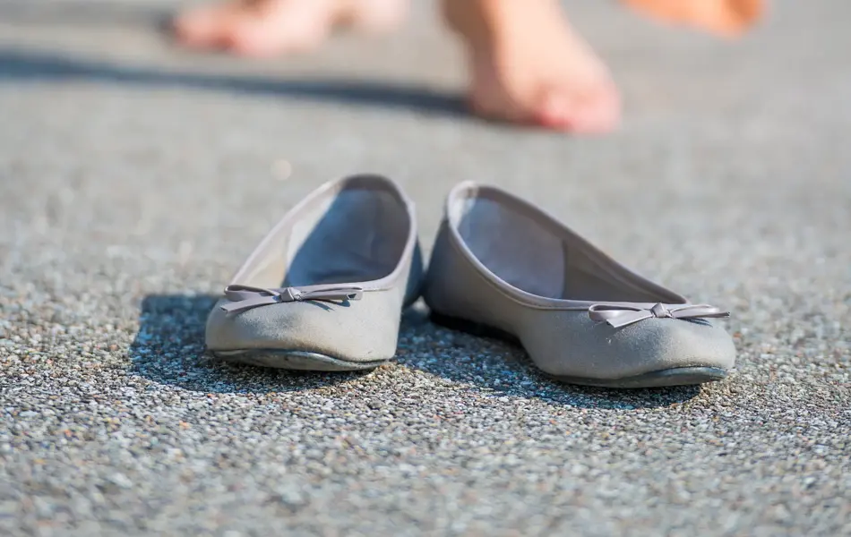 Nærbilde av lyse ballerinasko med sløyfe med dameben i bakgrunnen 