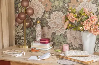 Et skrivebord med notatbøker, en lampe og en vase med blomster.