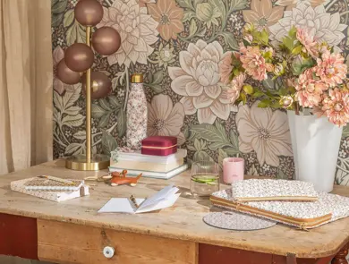 Et skrivebord med notatbøker, en lampe og en vase med blomster.