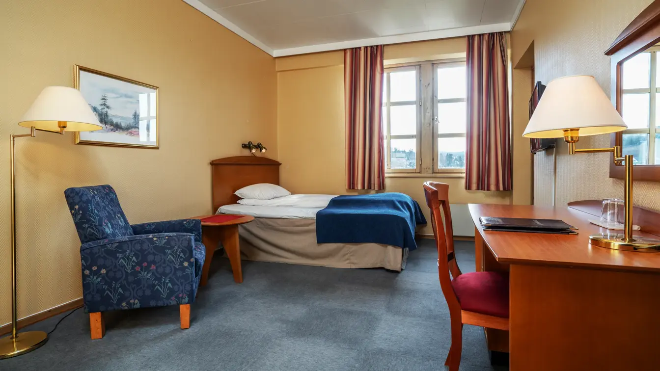 Mindre dobbeltseng med lenestol og skrivebord i mørkt tre