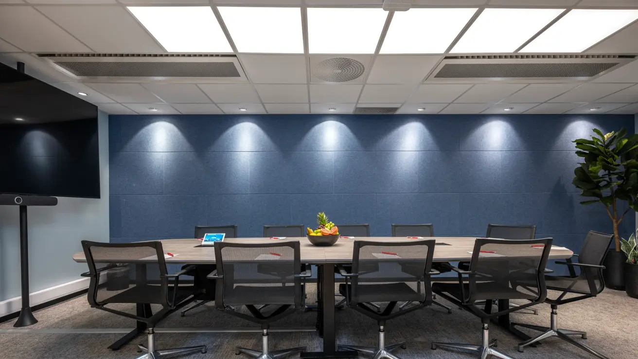 Møterom med styrebords oppsett til 10 personer. Blå vegg på langsiden og stor skjerm på veggen. 