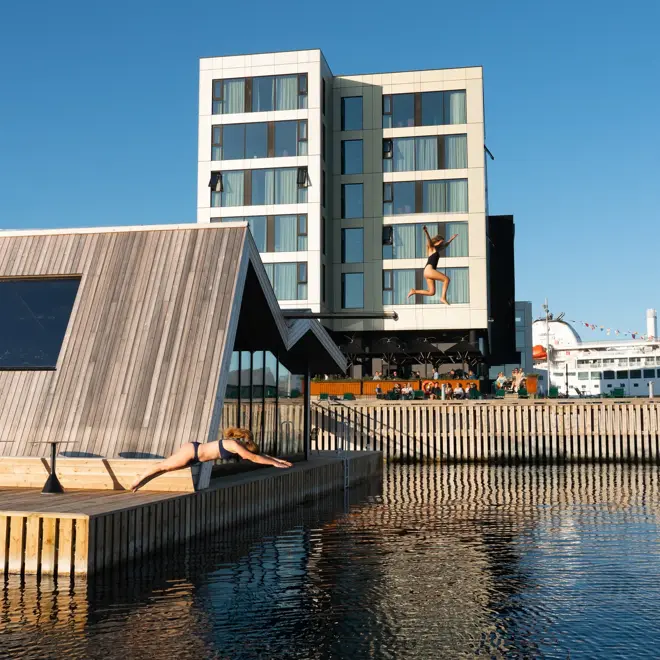 To kvinner stuper og hopper fra den flytende badstua utenfor Thon Hotel Svolvær.