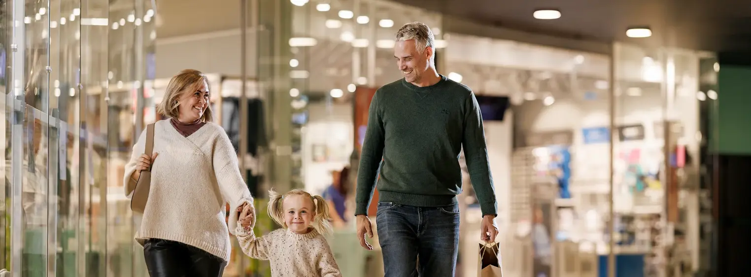 En mann, en kvinne og en liten jente går bortover en gang i et kjøpesenter