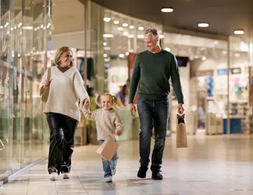 En mann, en kvinne og en liten jente går bortover en gang i et kjøpesenter