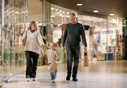 En mann, en kvinne og en liten jente går bortover en gang i et kjøpesenter