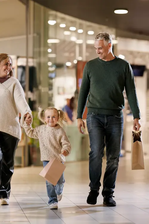 En mann, en kvinne og en liten jente går bortover en gang i et kjøpesenter