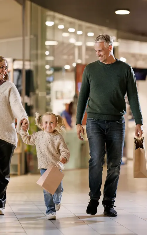 En mann, en kvinne og en liten jente går bortover en gang i et kjøpesenter