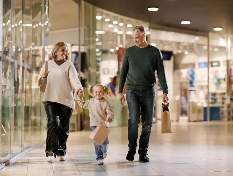 En mann, en kvinne og en liten jente går bortover en gang i et kjøpesenter