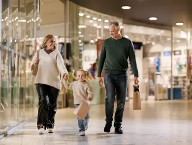 En mann, en kvinne og en liten jente går bortover en gang i et kjøpesenter