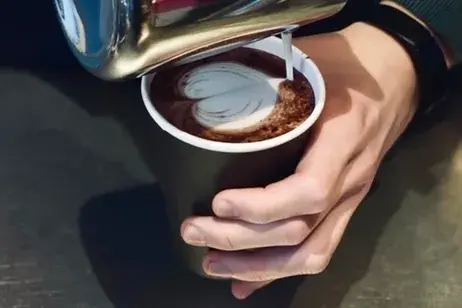 en hånd som heller kaffe i en kaffekopp og lager et hjerte av melkeskum