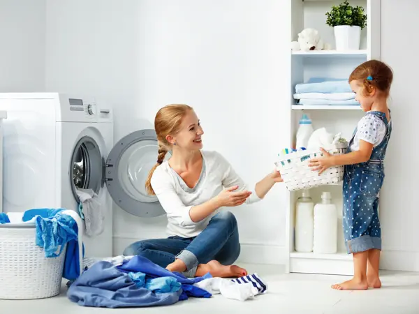 family mother and child girl little helper in laundry room near washing machine and dirty clothes