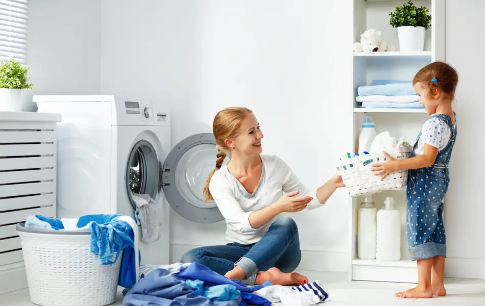 family mother and child girl little helper in laundry room near washing machine and dirty clothes