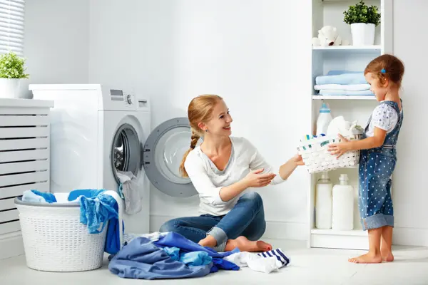 family mother and child girl little helper in laundry room near washing machine and dirty clothes