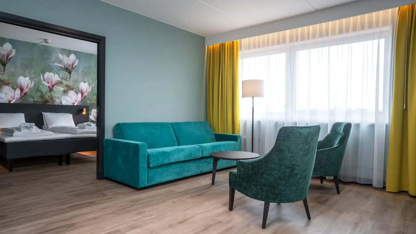 Blomstertapet, dobbeltseng, grønn sofa, stue, salongbord, to grønne lenestoler, vindu, gule gardiner, turkis/grønn vegg