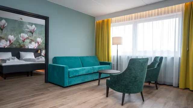 Blomstertapet, dobbeltseng, grønn sofa, stue, salongbord, to grønne lenestoler, vindu, gule gardiner, turkis/grønn vegg