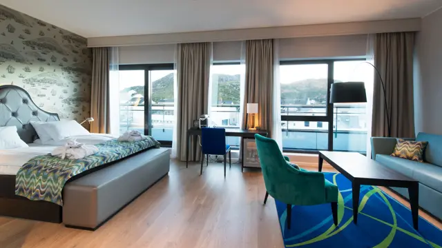 Dobbeltseng, arbeidspult og sittegruppe på businessrom på Thon Hotel Fosnavåg med utsikt utover havet