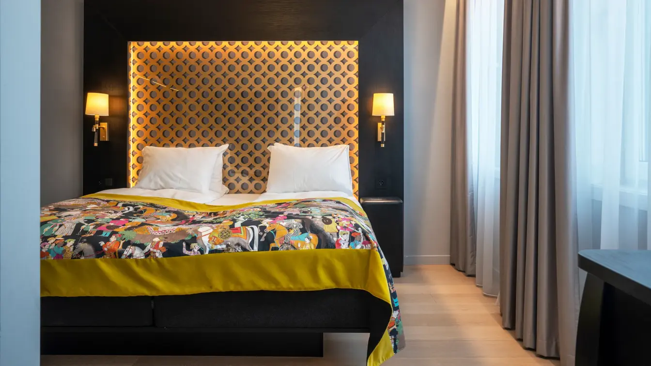 Dobbeltseng, vinduer, beige gardiner, parkettgulv, to nattbord med lamper 