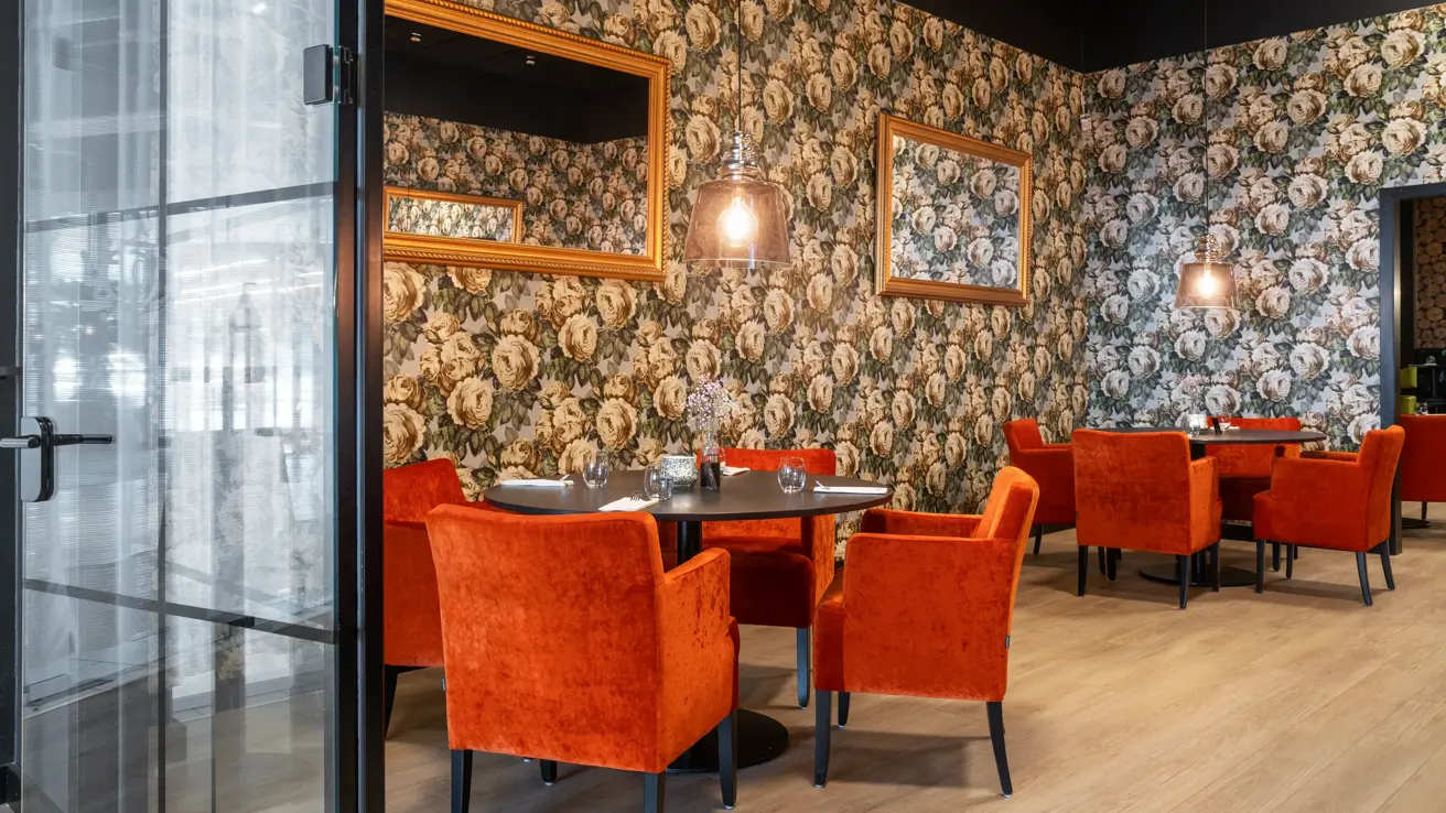 Tapetvegg, runde spisebord, oransje stoler, parkettgulv, veggspeil.