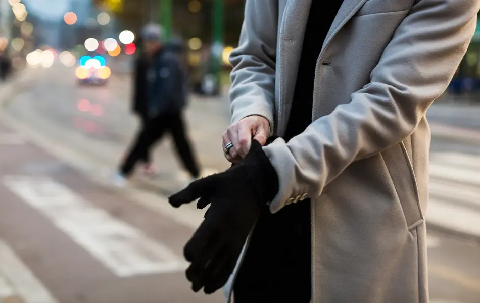 Nærbilde av mann med lys beige frakk som tar på hansker