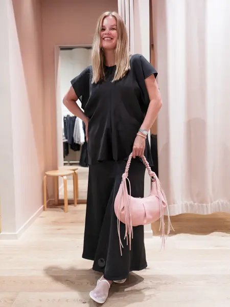 Damemodell med sort topp og sort langt skjørt og rosa veske.