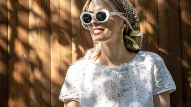 Portrait of a pretty girl in glasses and a headscarf standing against a wooden fence in the backyard on a Sunny day. High quality photo