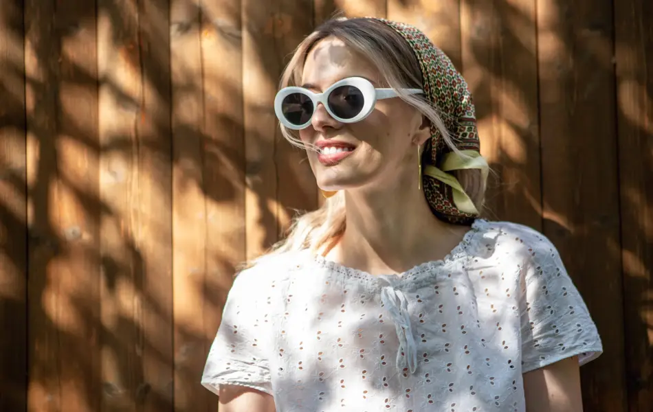 Portrait of a pretty girl in glasses and a headscarf standing against a wooden fence in the backyard on a Sunny day. High quality photo