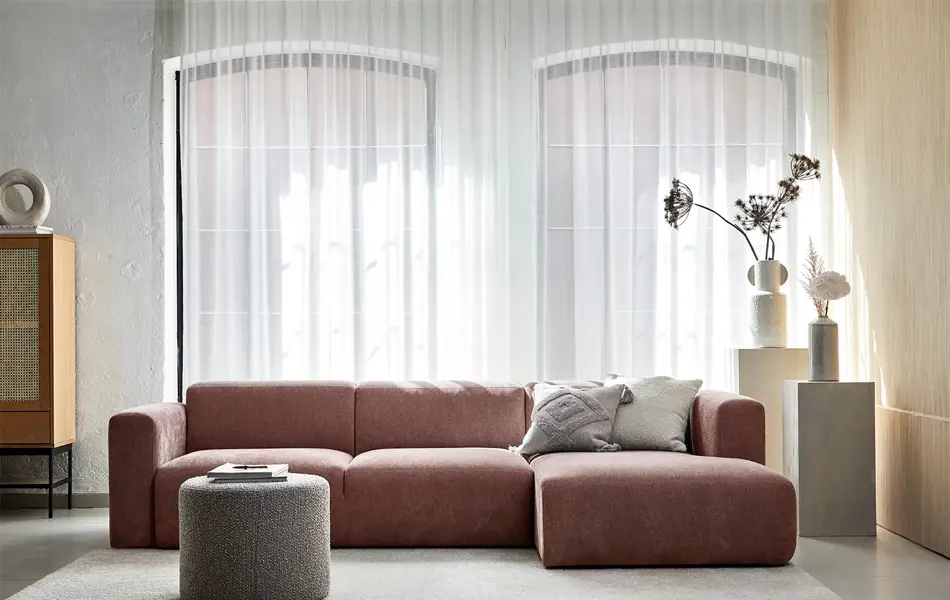 Stue med store vinduer og en rødlig sofa