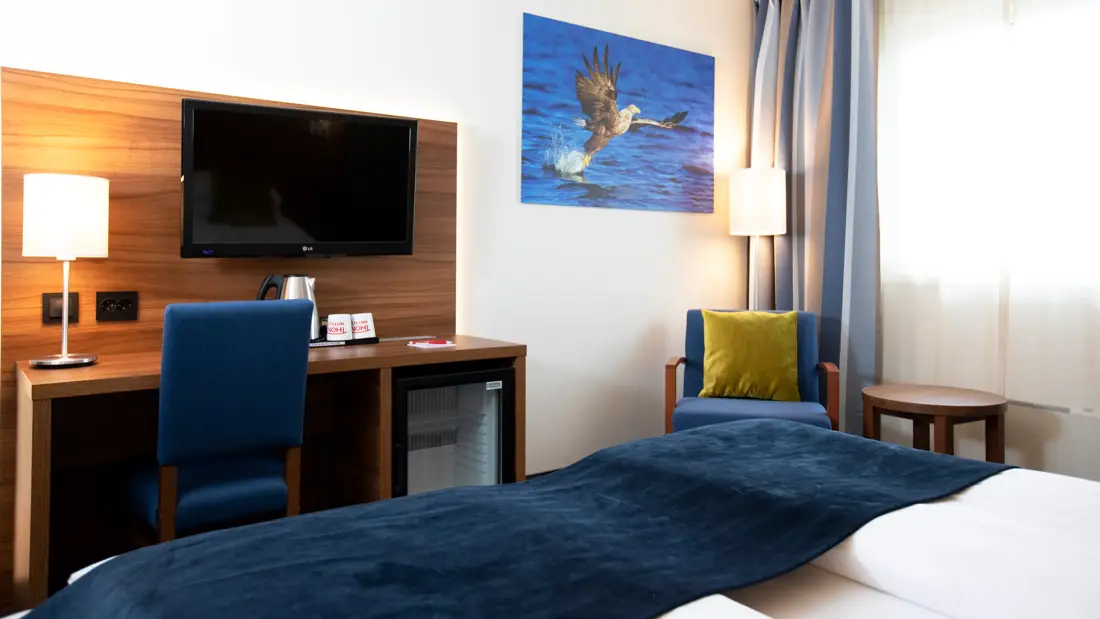 Skrivebord, TV, lenestol, bilde og sengekant i dobbeltrom