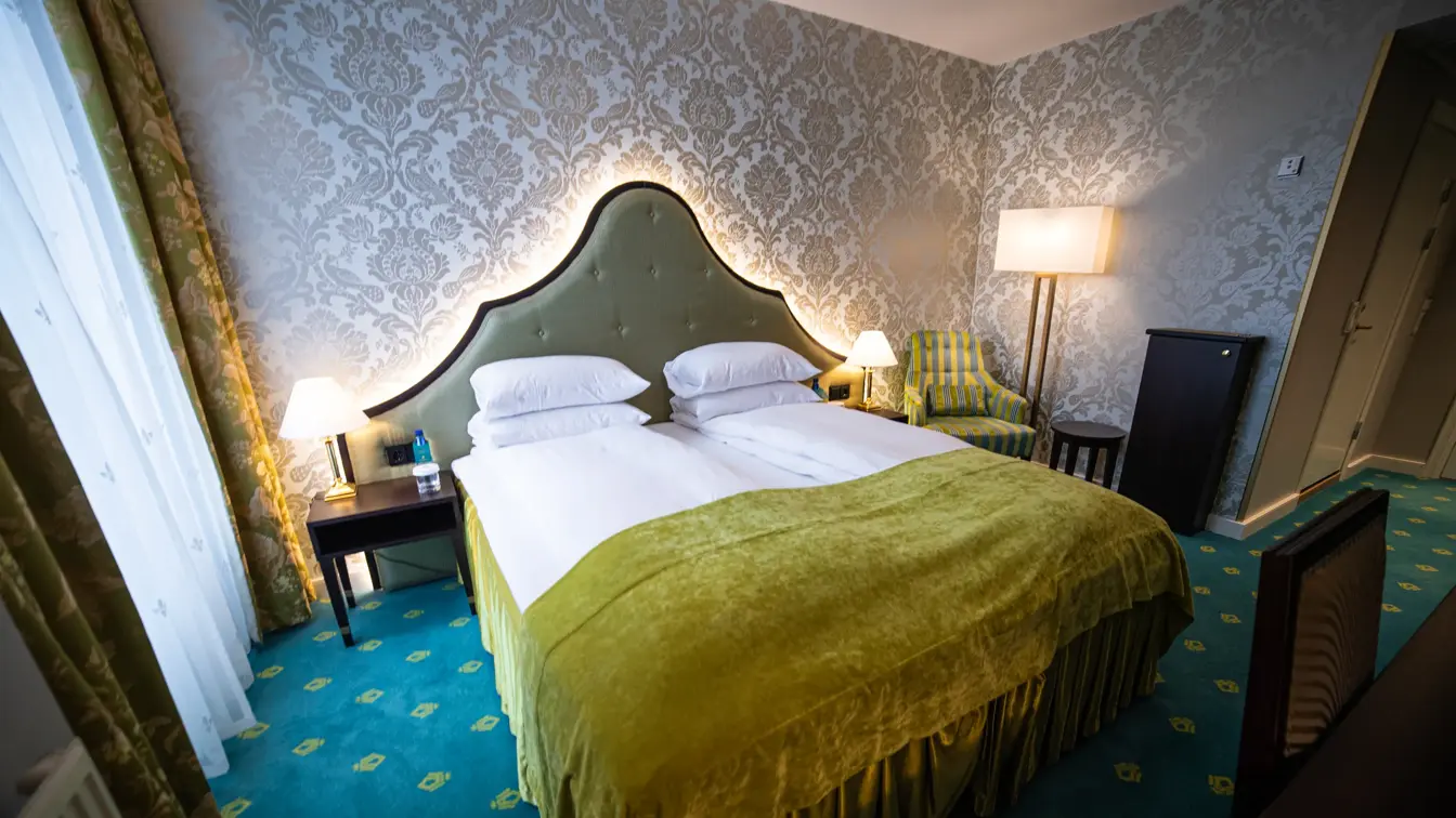 Dobbeltseng med nattbord, lenestol, tapet på vegg og teppegulv