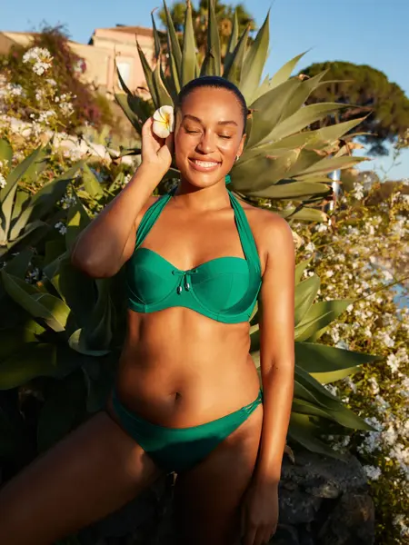 Modell ute foran grønne planter i en grønn bikini.