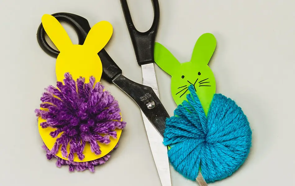 En gul og en grønn kanin laget av papir og garn ved siden av en saks 