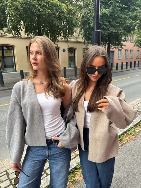 dame i grå genser, hvit skjorte og jeans, og dame i brun jakke, hvit skjorte og jeans