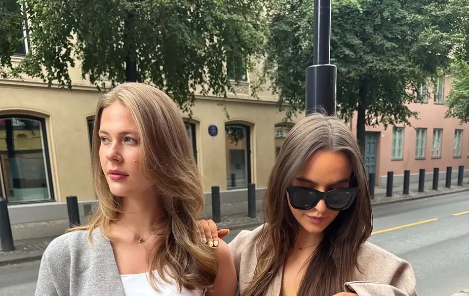 dame i grå genser, hvit skjorte og jeans, og dame i brun jakke, hvit skjorte og jeans