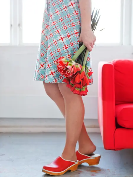 Dameben med røde klogger og blå kjole holder røde blomster sett fra livet og ned 