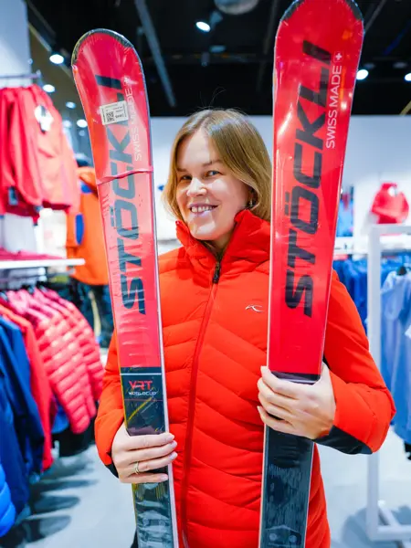 Jente med orangesekk og blådunjakke, og langrennski og slalåmski