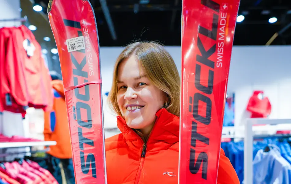 Jente med orangesekk og blådunjakke, og langrennski og slalåmski