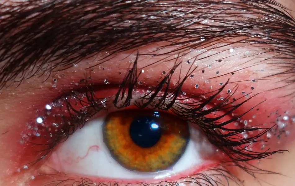 Nærbilde av øye sminket med rød øyenskygge og sølvglitter