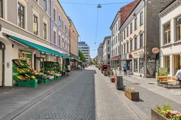Handlegaten Torggata, sett fra øst til vest. Gågaten er pyntet med blomsterkasser og brostein. En grønnsakshandel på venstre side og restauranter med uteservering på høyre side.