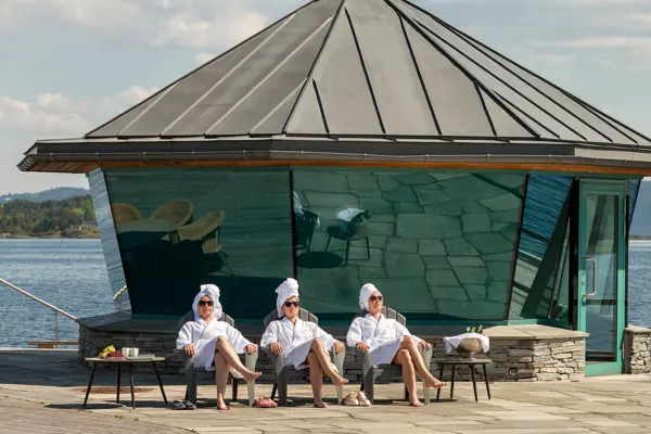 Tre mennesker i badekåpe sitter foran Fjordhotell badehus