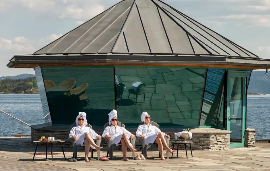 Tre mennesker i badekåpe sitter foran Fjordhotell badehus