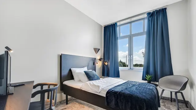Enkeltseng, hvite vegger, TV, skrivebord, stol, lenestol, vindu, blå gardiner