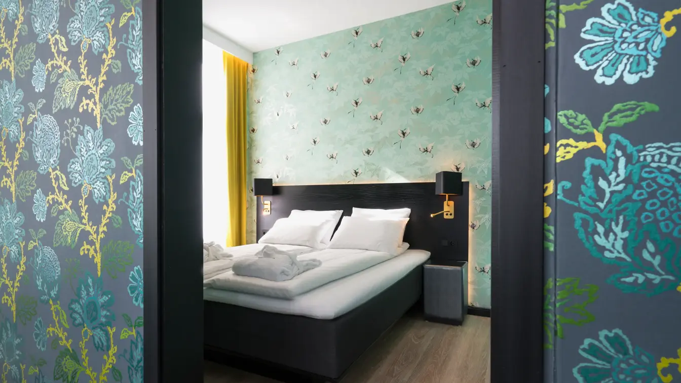 Businessrom med stilfull tapet, dobbeltseng og gule gardiner